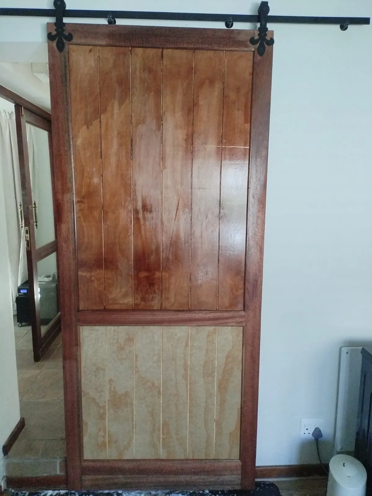 Timber barn door hanging on a black steel top track with decorative cast hangers, part-way through staining