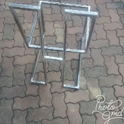 A pair of bare stainless stool frames laid on paving, showing the repeated cantilever geometry