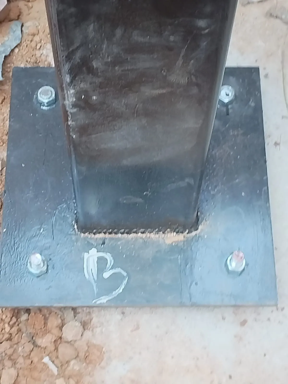 Close-up of a column base plate: the column welded right around its perimeter and bolted down through four anchors