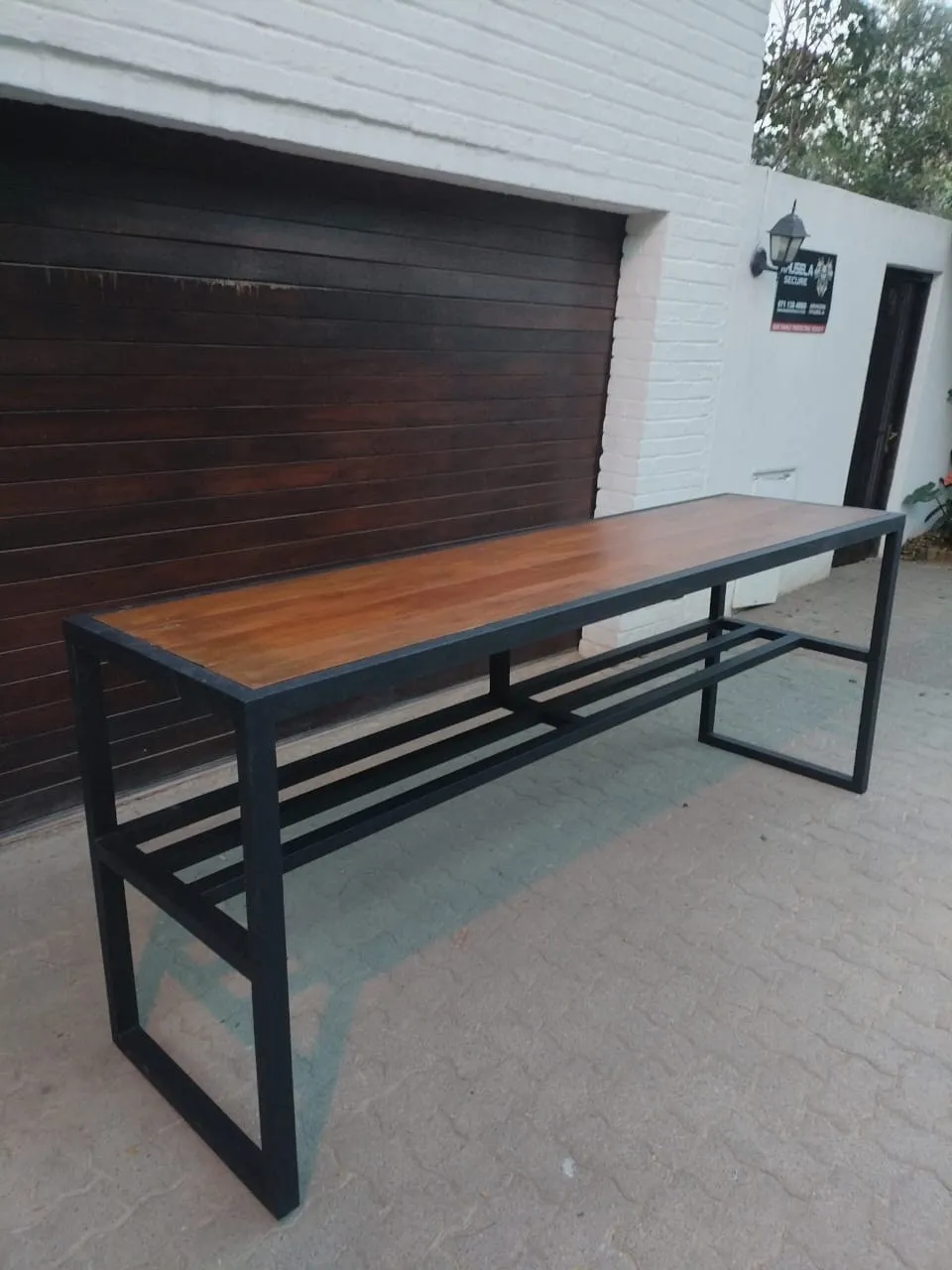 Finished console table with a matt black steel frame and a stained hardwood top, standing on a paved driveway