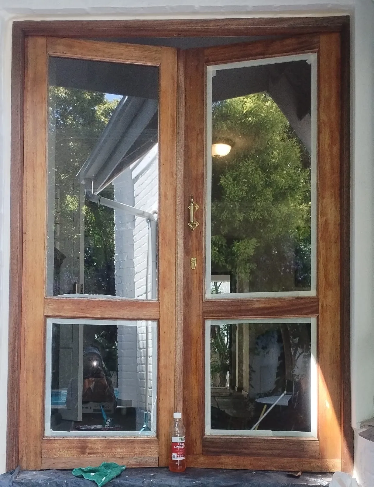 The french doors part-way through restoration, sanded back with dried-out patches still visible and a bottle of raw linseed oil on the sill