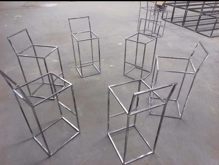 A batch of stainless steel stool frames grouped together on a workshop floor, all built to the same pattern
